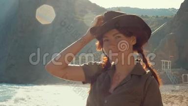 一个美丽的红发旅行女孩戴着牛仔帽在海边的肖像。